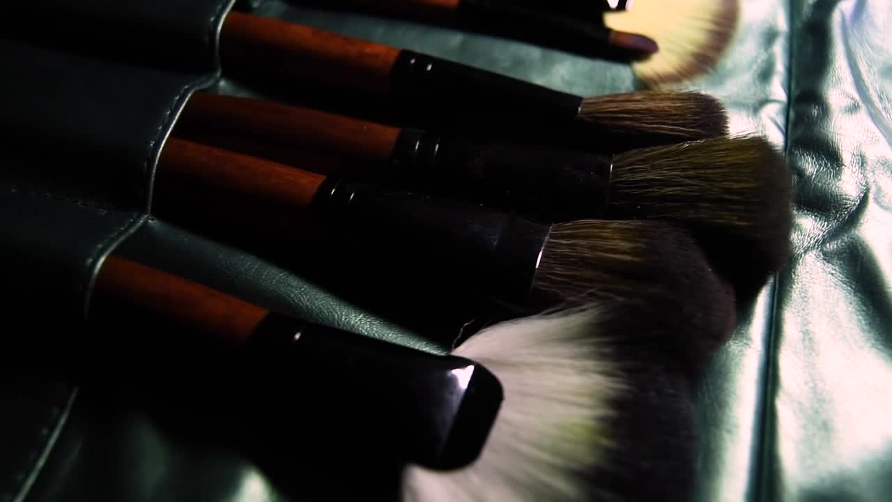 Træ- og metalbrune makeupbørster på grøn skinnende baggrund med glidende bevægelse.