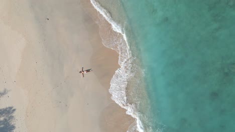 woman lying on golden sandy beach during sun is shining and splashing waves of seashore in gili island