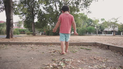 clip en cámara lenta de un niño asiático de dos años caminando descalzo sobre la arena y hojas secas en un parque al aire libre con libertad y ambiente salvaje