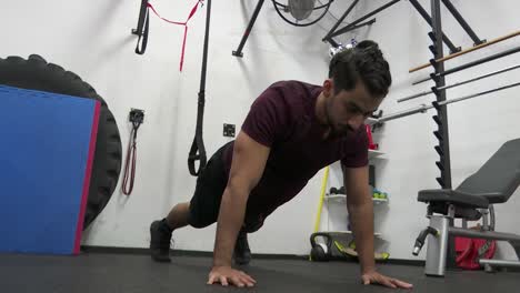 un hombre de pelo oscuro y barba hace flexiones y se mantiene justo por encima del suelo