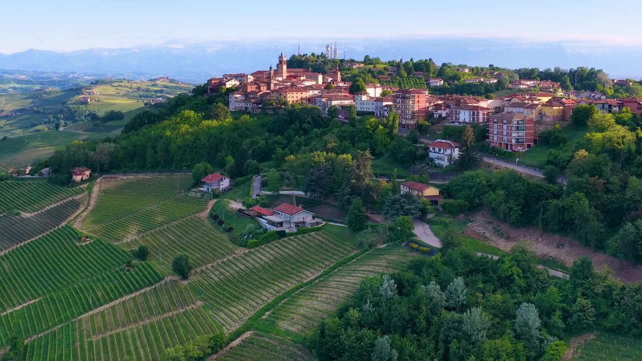 Riprese con drone rivelano un villaggio storico in cima a una collina circondato da dolci vigneti verdi e montagne.