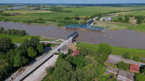 wide drone shot of the friesenbrücke construction over the ems river in germany, including the future railway access road. highlights the lift-swing mechanism and surrounding rural infrastructure.