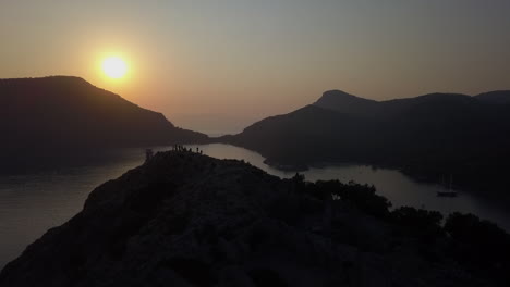 aerial flyover: tourists gather on mountain top to view ocean sunset