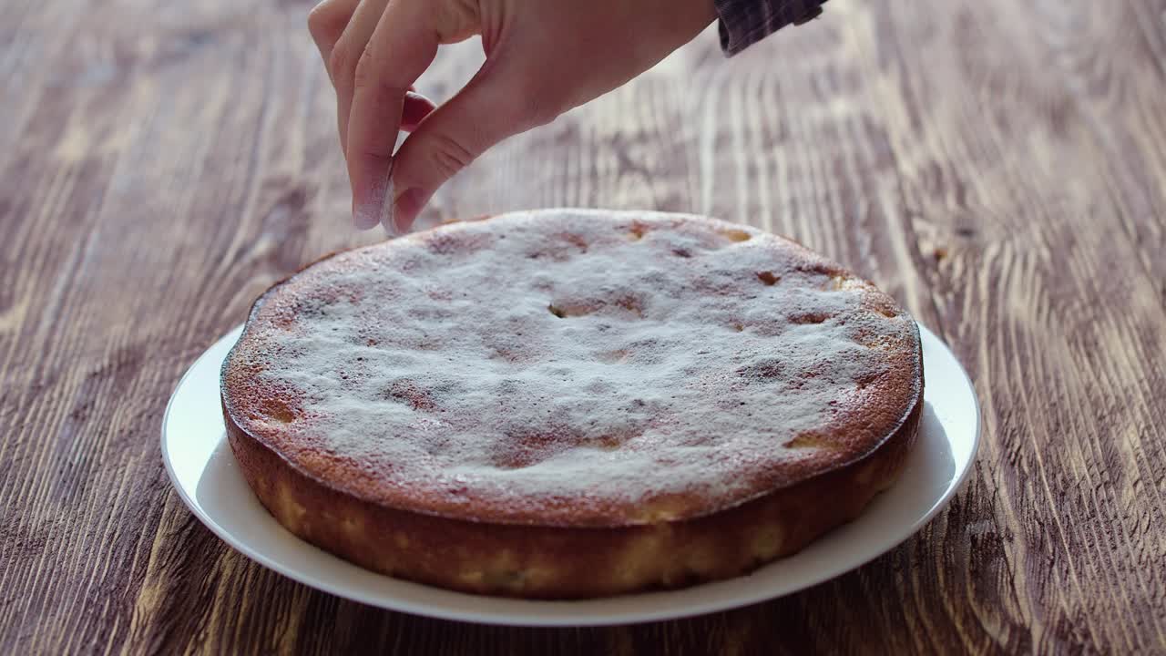la mano de una mujer salpica una tarta de manzana con azúcar en polvo. video en primer plano