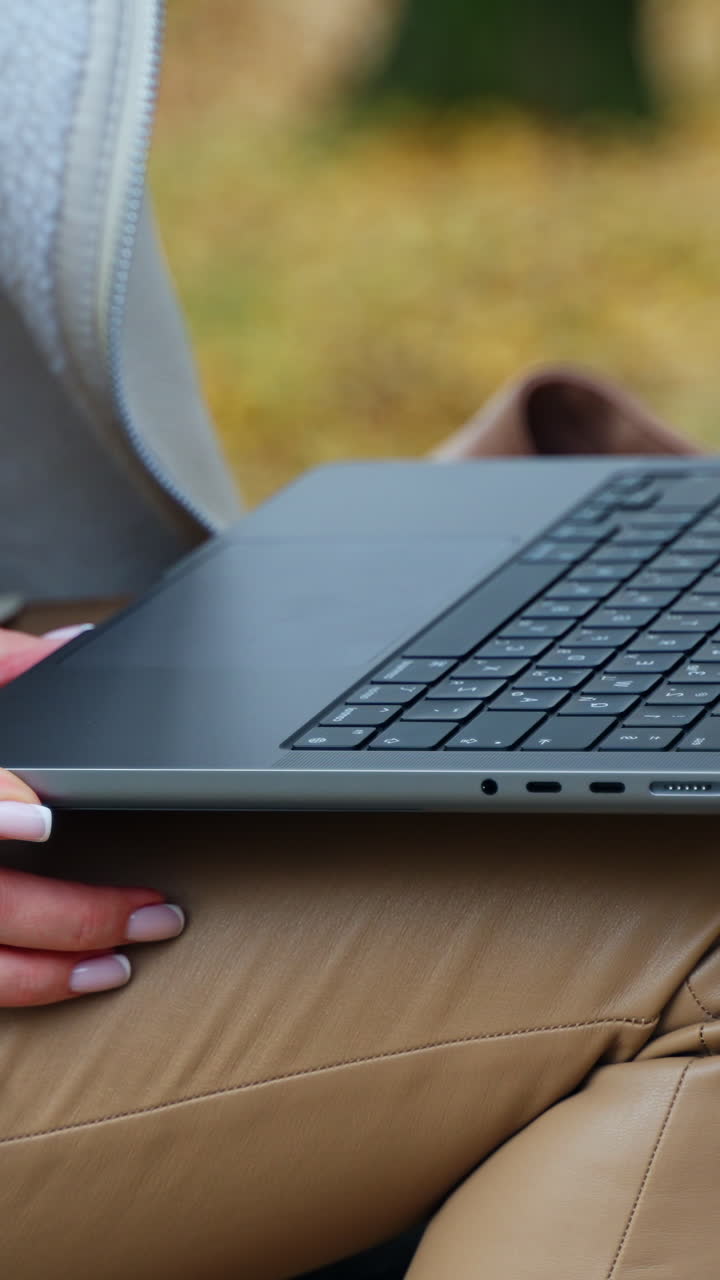 Female hands open laptop lying on the knees in beige pants. Lady sitting outdoors is going to work out of office. Vertical video