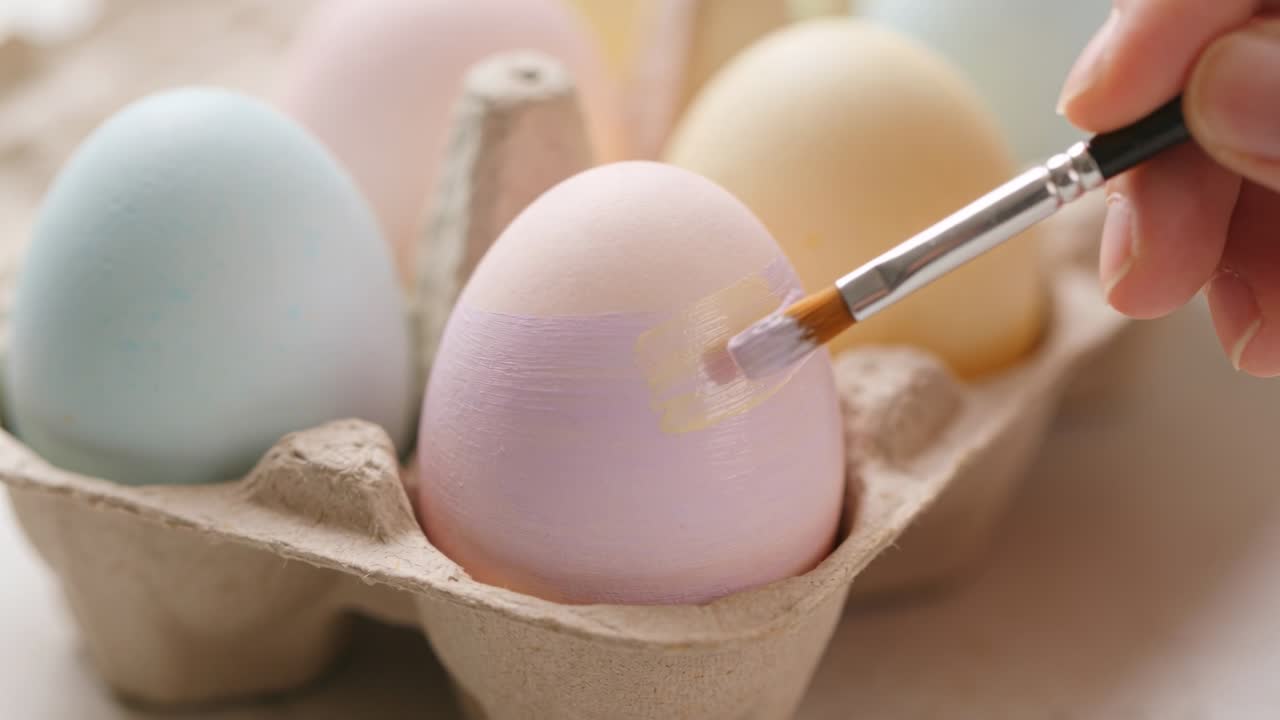 Painter brushing pastel egg from right and applying layered lavender patch for craft demo