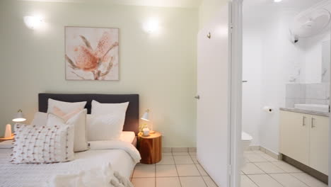 small modern tiled apartment bedroom reveal past doorframe to en suite bathroom with marble cabinetry and glass shower