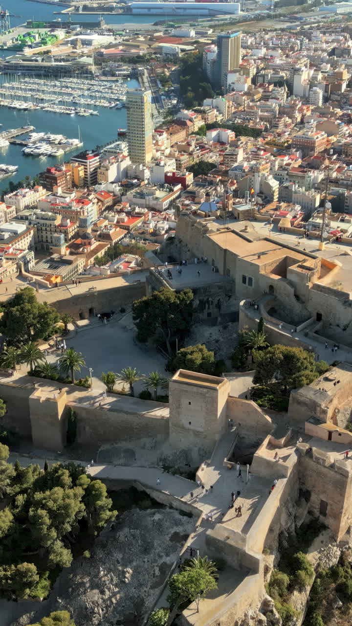 Luftdronebillede af Santa Barbara-slottet på kysten af Alicante, Spanien med byen og havet i baggrunden. Lodret
