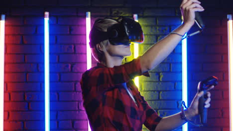 young woman in vr glasses and using joystick while playing a virtual reality game in a room with colorful neon lamps on the wall 4