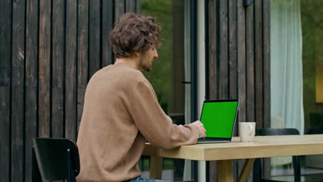 hombre trabajando al aire libre en una mesa de madera con una computadora portátil