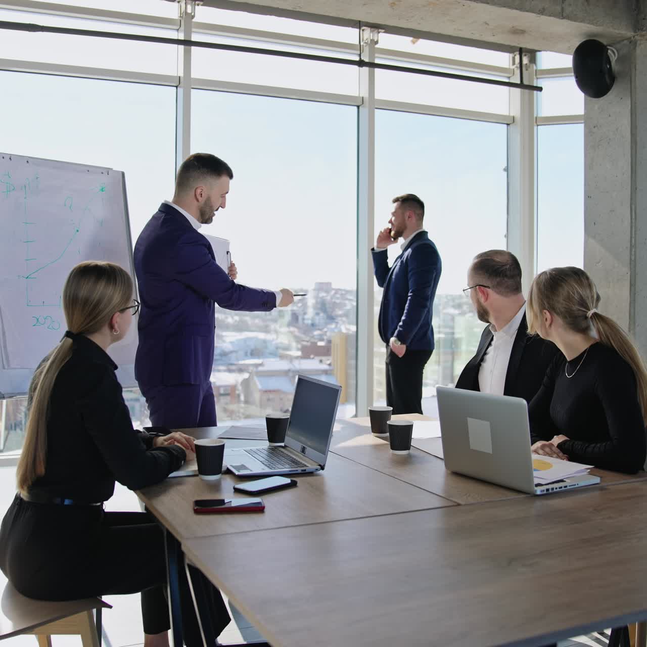 Coworkers' team discussing the chart in the hands of their chief. Active collaboration in the office atmosphere. Male businessman speaking on the phone at the backdrop