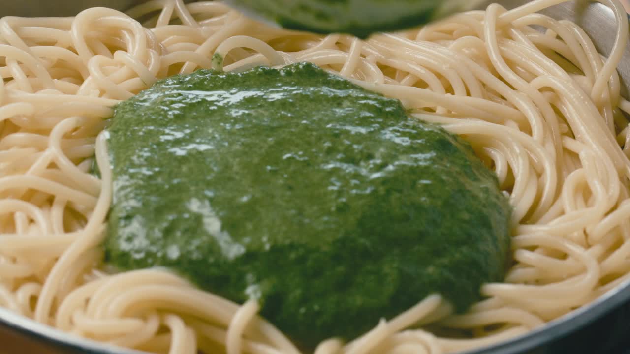 Adding Spinach Sauce to Spaghetti and Stirring with Kitchen Tongs