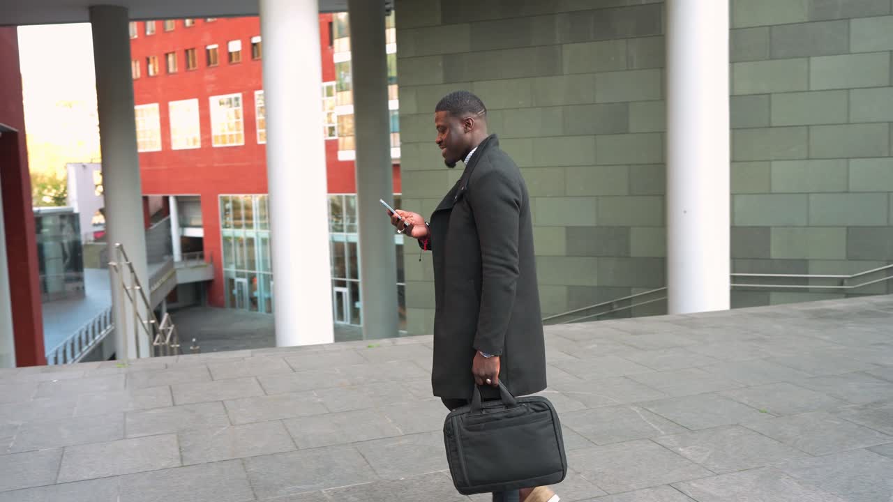 Man in coat walking and texting with a briefcase