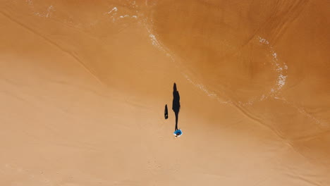 Schatten-Einer-Person,-Die-Am-Sandstrand-Von-Portugal-Mit-Reichen-Wellen-Ein-Handtuch-Schwenkt---Luftaufnahme-Von-Oben-Nach-Unten