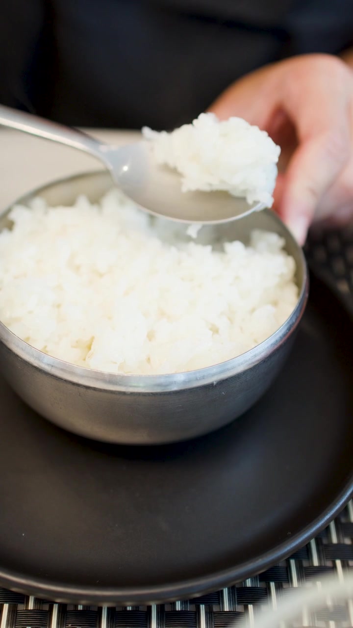 ある人が金属製の蒸しご飯の器を開け、スプーンで食べ始める