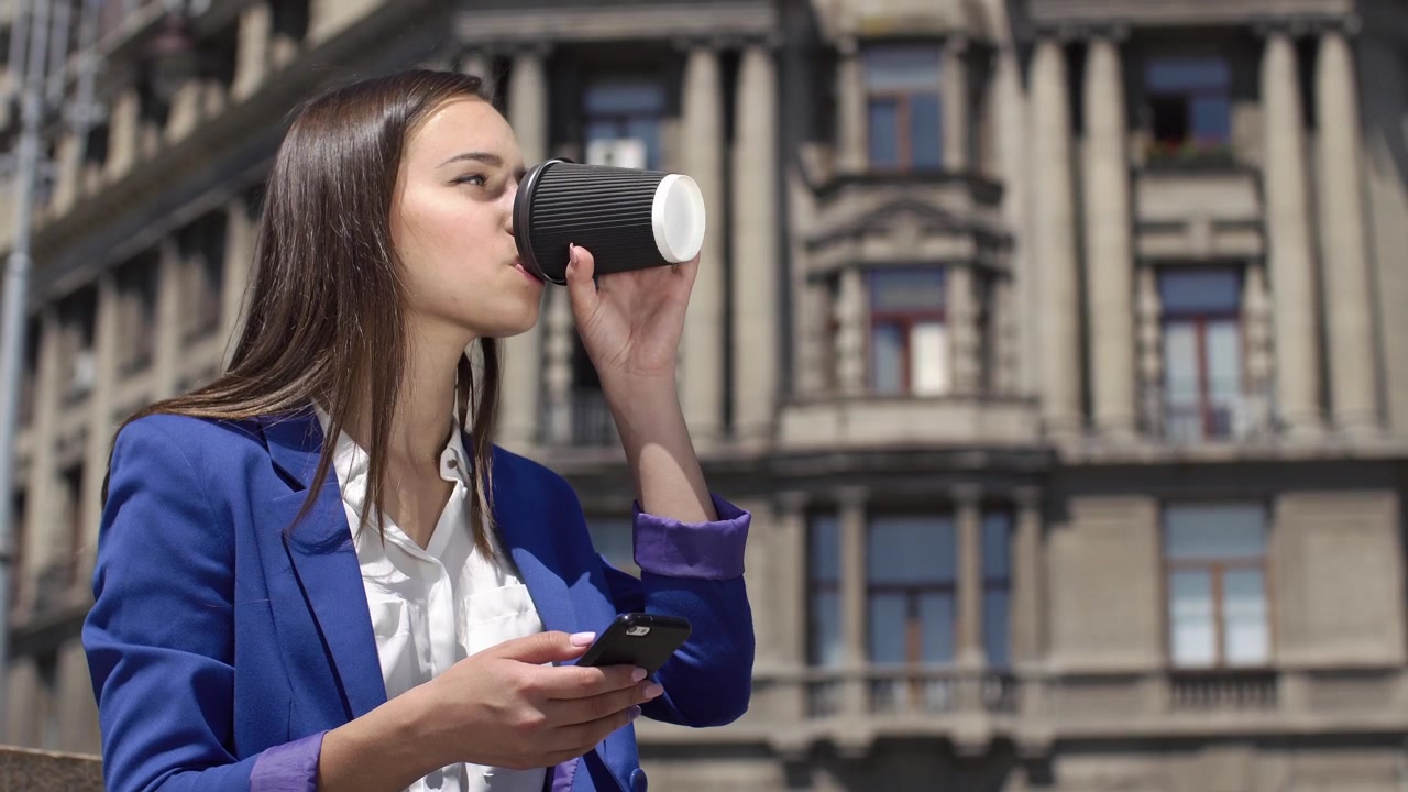 Giovane imprenditrice che usa lo smartphone e beve caffè all'aperto