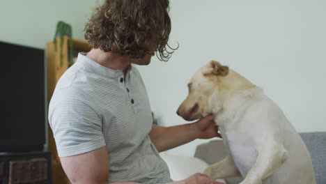 hombre discapacitado caucásico feliz en silla de ruedas jugando con un perro mascota en la sala de estar