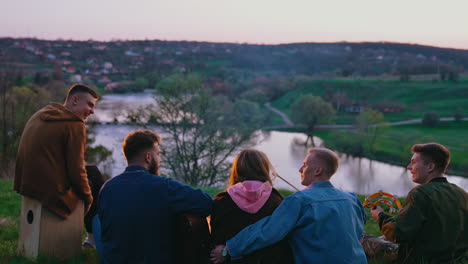 young people have a picnic in the evening. group of friends spending happy time by the fire on beautiful nature background. rear view.