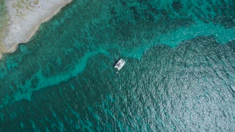 Vista-Aérea-De-Drones-De-Arriba-Hacia-Abajo-De-La-Isla-Desierta-De-Bahamas-Con-Un-Velero-Solitario-Y-Agua-Cristalina