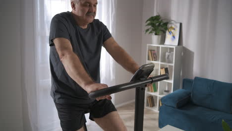 Gesunder-Mann-Mittleren-Alters-Trainiert-Am-Wochenende-Zu-Hause-Mit-Dem-Spinning-Bike-Und-Tritt-In-Die-Pedale,-Um-Im-Wohnzimmer-Cardio-Training-Zu-Machen