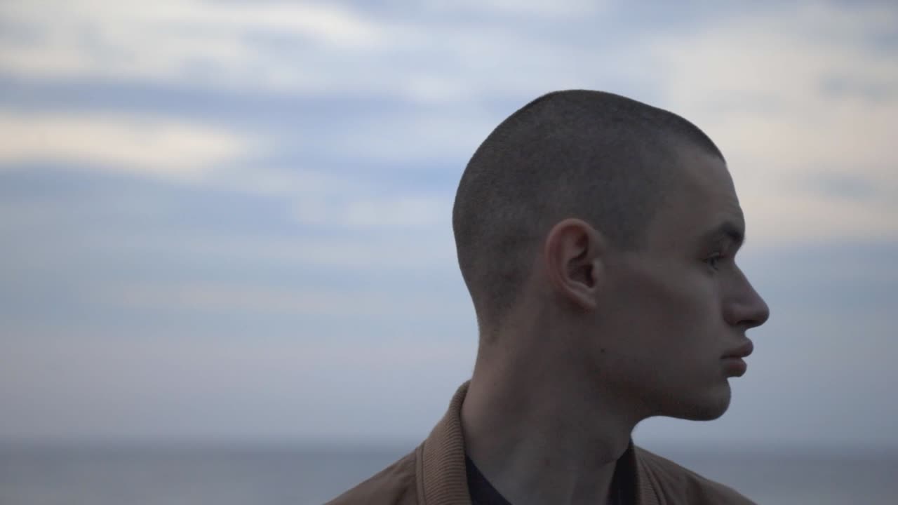 Portrait Of A Man Turning His Head Looking Around The Beach Against Cloudy Sky Background - Closeup Shot