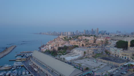 wide parallax view drone shot of old city of jaffa and jaffa port at sunset with lots of families visiting restaurants, shops and bars in the port - tel aviv city at the background