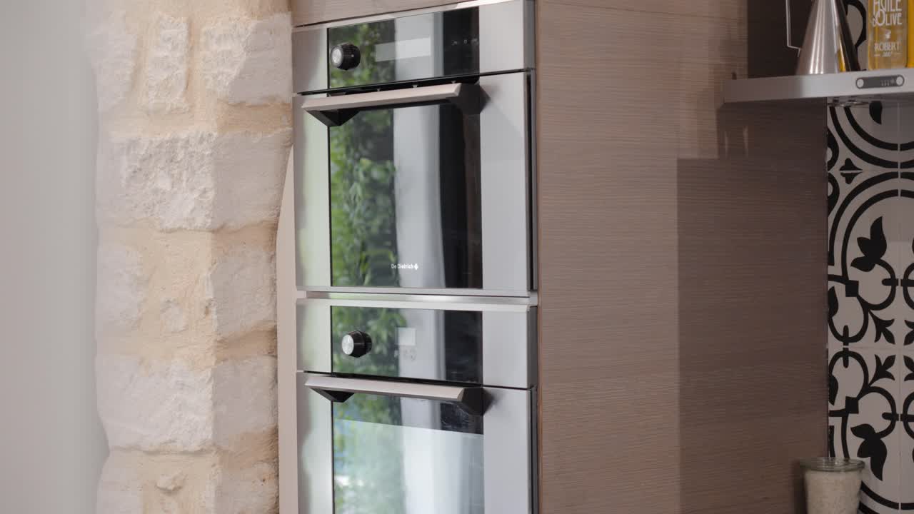 Modern kitchen featuring sleek double ovens against a rustic stone wall and patterned backsplash.