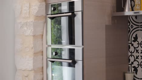 modern kitchen featuring sleek double ovens against a rustic stone wall and patterned backsplash.