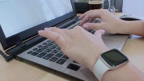Close-up of hands typing on laptop, smartwatch on wrist.