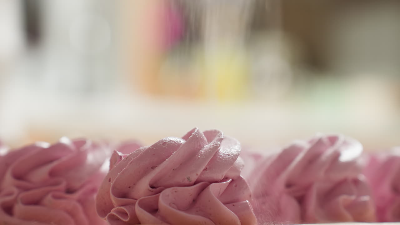 Close up of swirl pink cupcake with sugar gently sprinkled over top, sitting on parchment paper with soft blurred background, highlighting creamy texture, pastel color, and delicious dessert