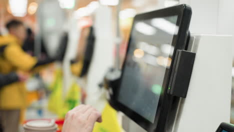 person interacting with a touchscreen interface on a machine in a busy environment, showing blurry people in the background