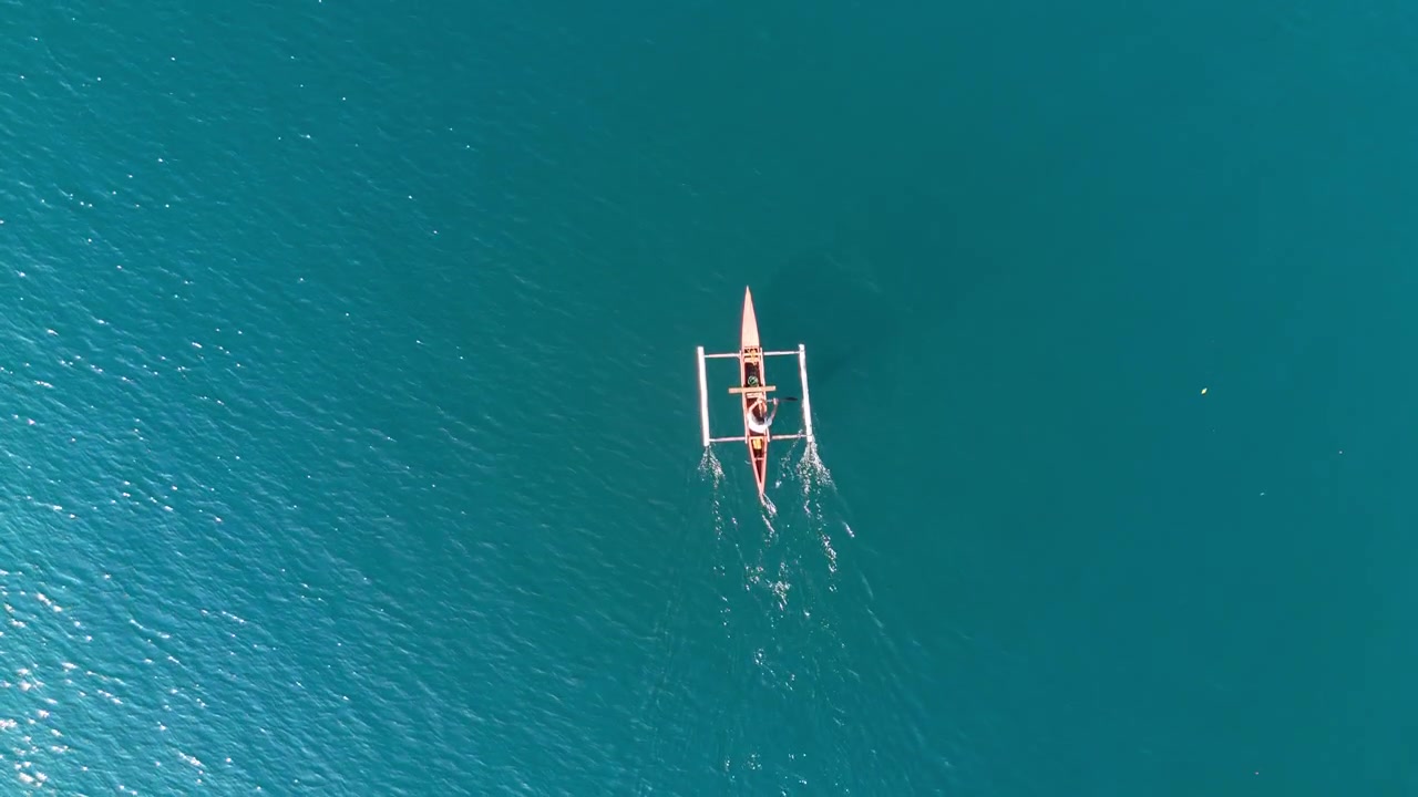 Sporingsoptagelse fra drone ovenfra af en fisker, der padler en lille rød udliggerbåd over det rolige hav ved Liminangcong, Filippinerne