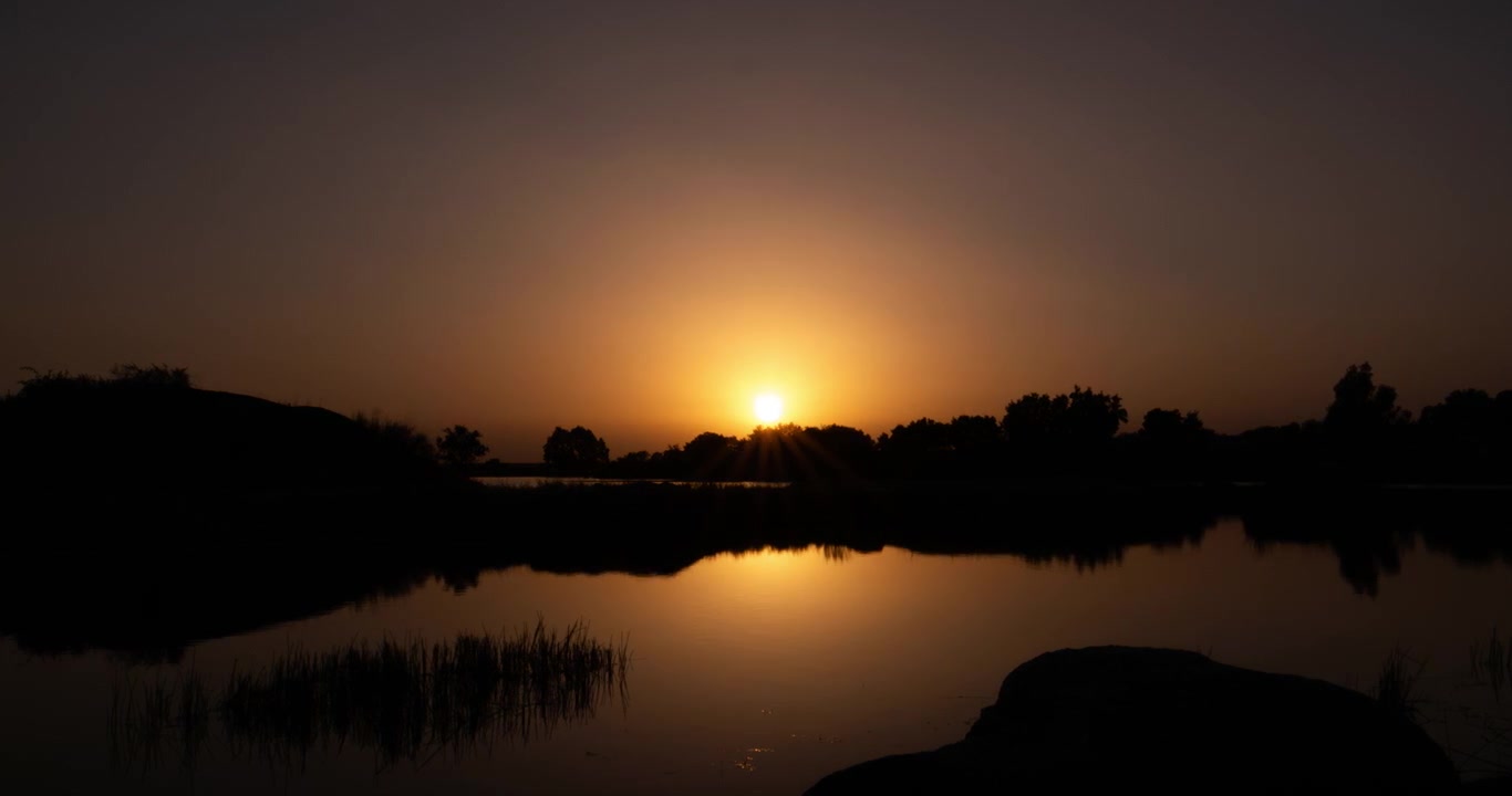 Aikaviivevideo kultaisesta auringonlaskusta, joka heijastuu tyynestä vedestä.