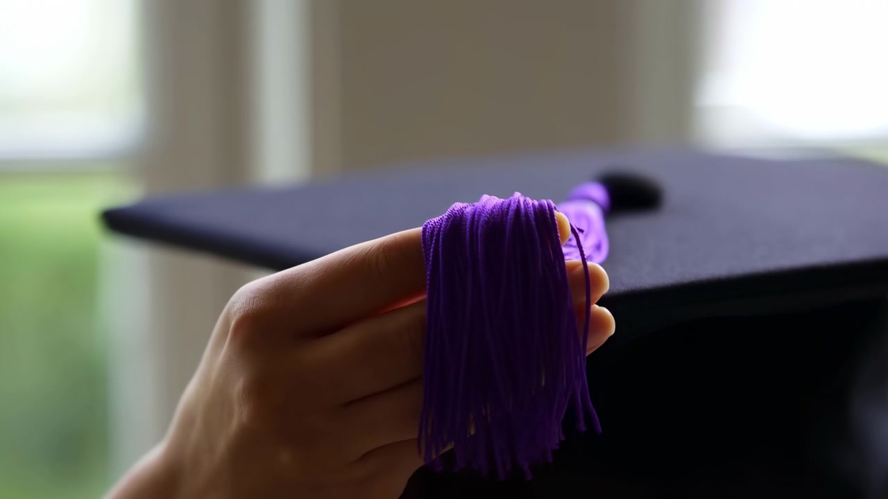 Chapeau de diplômé ajustant le gland, en intérieur près d'une fenêtre, avec un chapeau de diplômé, un gland violet, avec une texture de papier, de ficelle, d'une perspective en gros plan légèrement au-dessus, avec des accents noirs, violets