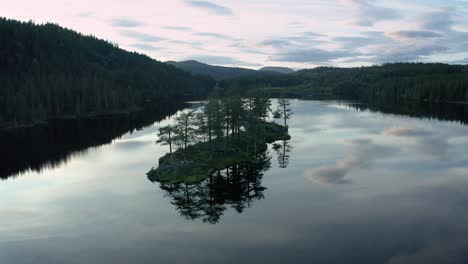 perfect mirror image in calm lake water of small island with trees, aerial dolly