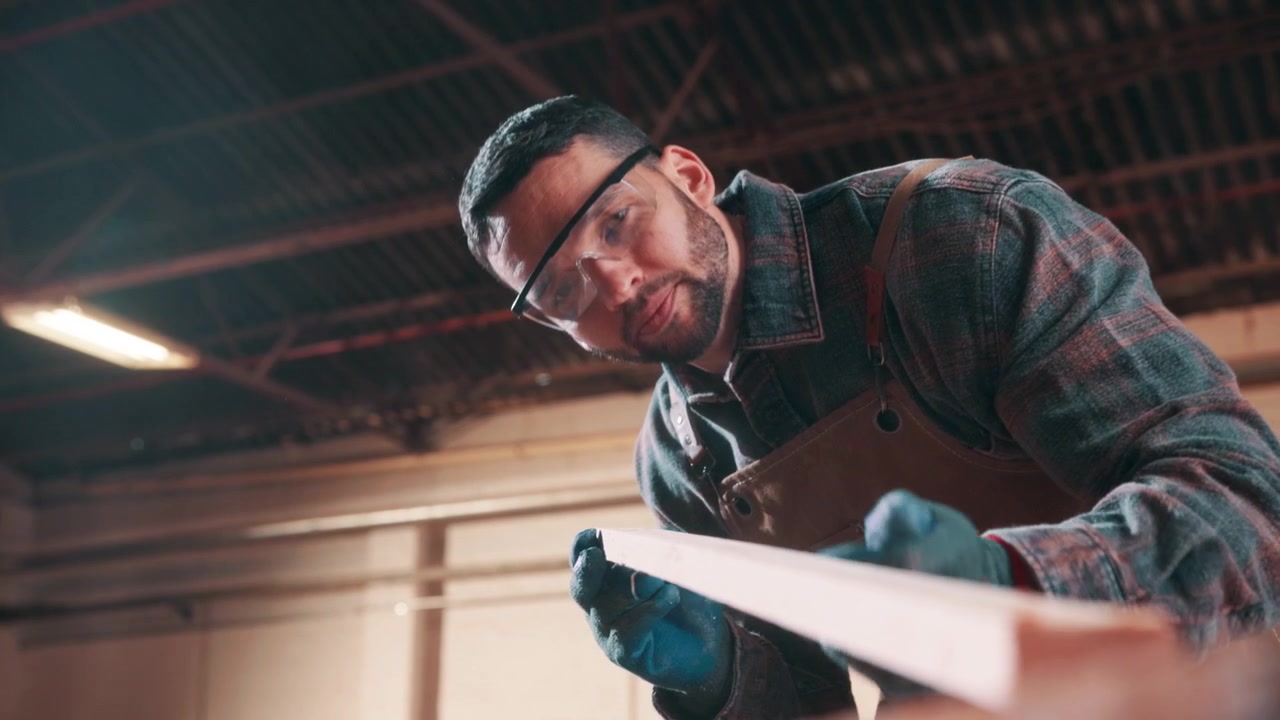 Carpenter Inspecting and Cleaning Wood Plank in Workshop