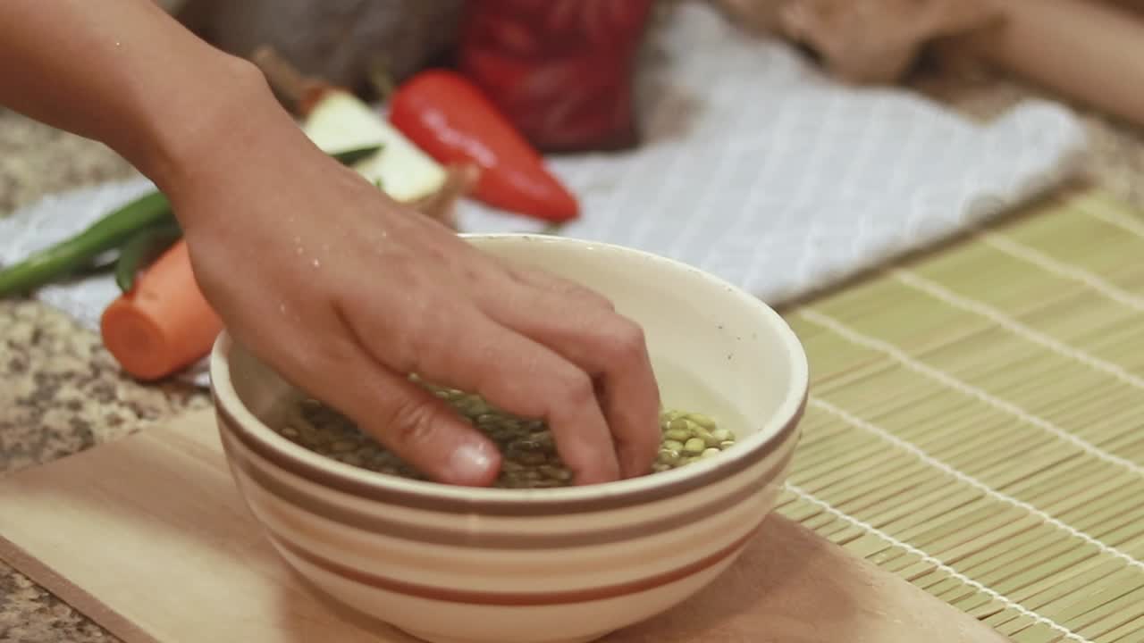 Hands rinsing raw organic mung beans in a bowl of water, cooking ingredient preparation