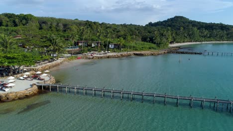 aerial, pan, drone shot of buildings on the coast and wooden piers, in turquoise sea, at a paradise beach, on a sunny day, in koh kood, thailand