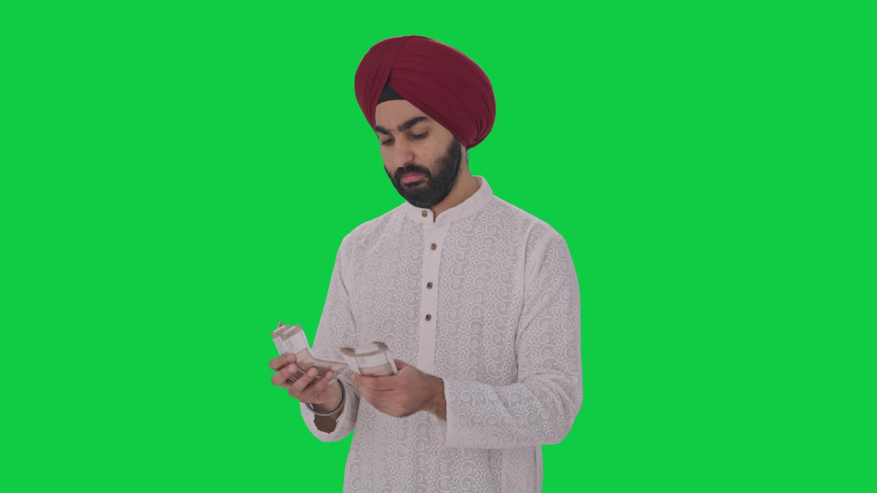 Uomo indiano sikh che conta denaro su schermo verde.