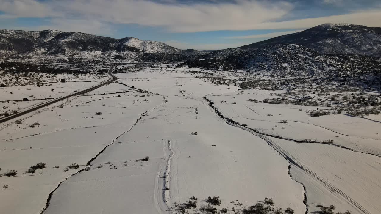 vuelo de avión no tripulado en una llanura nevada viendo ranuras en la nieve creadas por corrientes de agua y hay una carretera en un lado sin vehículos con un fondo de montañas en invierno en ávila, españa