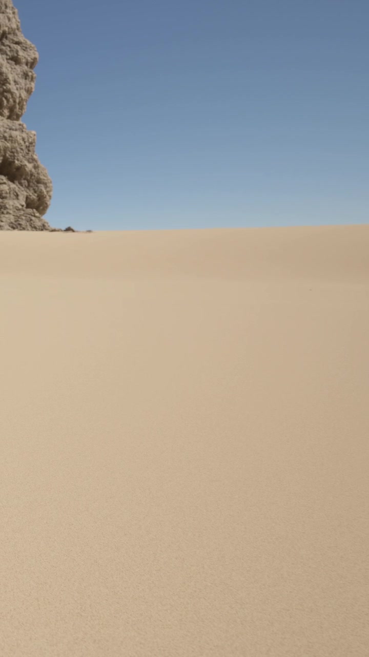 Paesaggio di dune di sabbia sotto un cielo sereno in un vasto deserto durante le ore diurne.