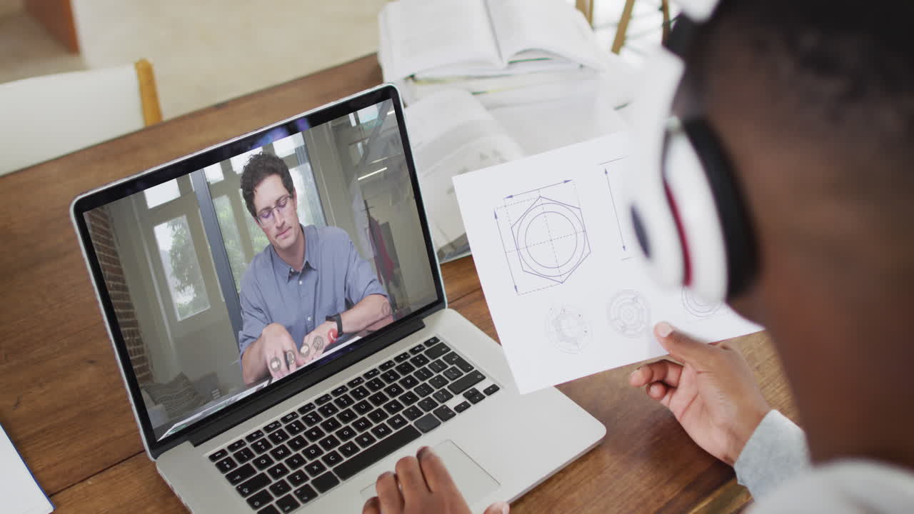 estudiante universitario afroamericano que sostiene notas mientras hace una videollamada en una computadora portátil en casa