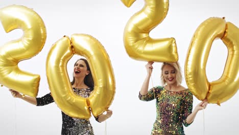 mujeres con globos dorados construyendo la figura "2020"