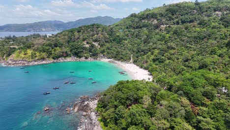drone footage captures a serene beach cove in phuket, thailand, showcasing turquoise waters, lush greenery, and a tranquil atmosphere