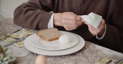 midsection of man wiping hand with tissue paper before having bread and egg at table