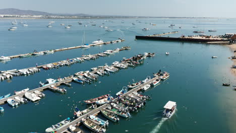 aerial orbiting shot showing port of olhao and fishing boat leaving harbor for fishing during bright sunny day in portugal