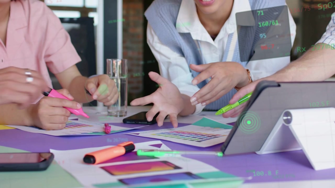 Il team di design si riunisce attorno a campioni di colore, indicando un tablet e scegliendo una palette per il marketing