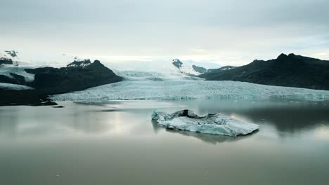 Glacier-melting-due-to-global-warming-with-icebergs-drifting-on-its-surface,-Snow-peaks-in-the-background,-Iceland,-Slow-motion-drone-shot