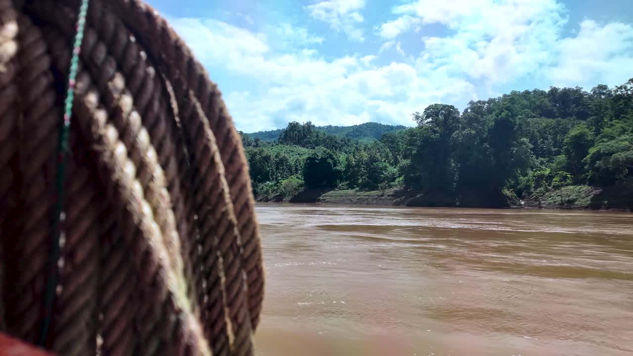 Cuerda colgando de un barco lento que viaja por el río Mekong con un exuberante paisaje selvático