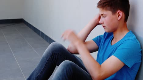 triste escolar sentado en el pasillo
